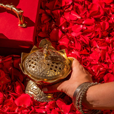 Lotus brass incense burner held by a hand on red rose petals with a red background