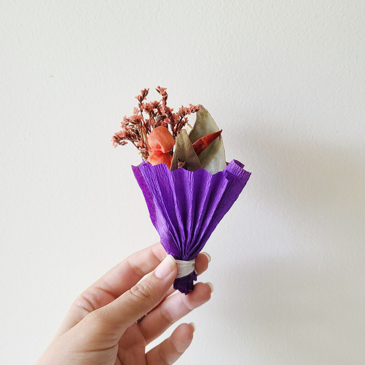 Hand holding a small bouquet of dried flowers wrapped in purple paper
